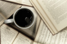 A cup of coffee sitting in a pile of open books
