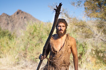 John the Baptist with a staff in the wilderness ready to baptize and prepare the way for the coming King. Voice of calling in the wilderness. Dedicated disciple and biblical character follower of jesus