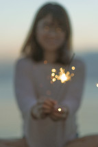 a young woman holding a sparkler on a beach 