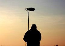 Silhouette of a production assistant holding sound equipment.