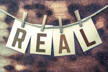 The word, "real," spelled out on cards hung on a string with clothespins.