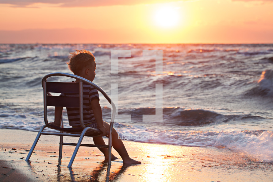 Little child looking at sunset sitting by the sea
