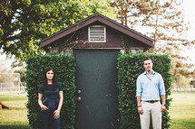 a man and a woman standing apart in front of a shed 