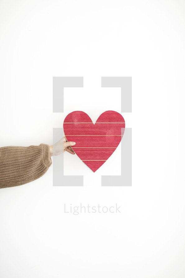 an arm holding out a wooden heart sign 