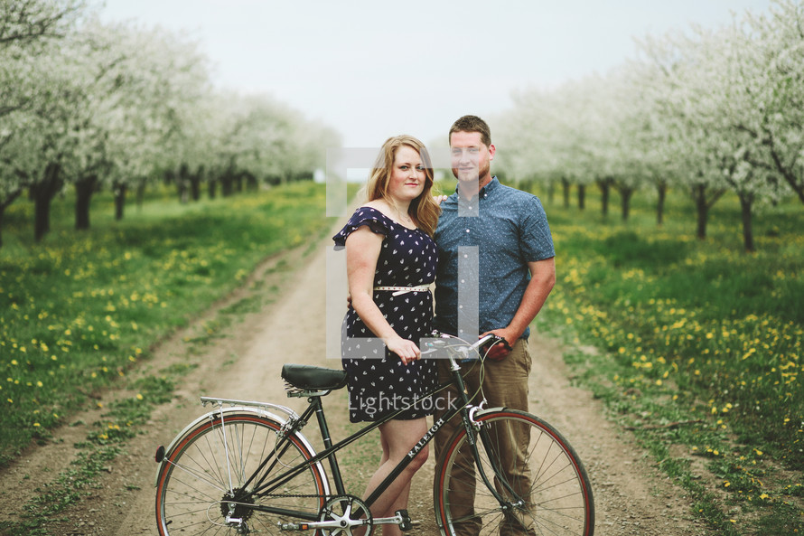 happy couple standing in an orchard with a bicycle 