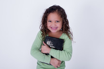 Smiling girl holding a closed Bible.