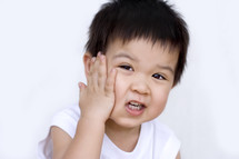 a toddler boy with his hand on his face 