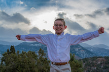 boy child with open arms with mountains behind him 