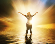 woman standing in water with her hands raised in the air surrounded by glowing light 