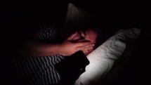 a man looking at a cellphone screen lying in bed at night 