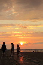 people walking on a jetty on a beach at sunset 