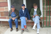 Three older men in overalls sitting outside on a bench.
