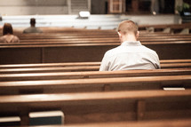 Man praying while sitting in a church pew.