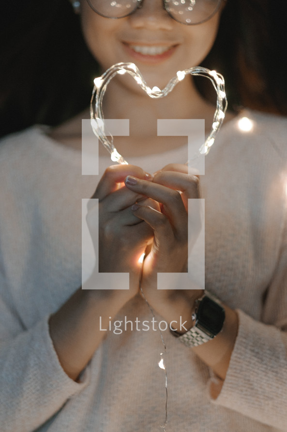 a young woman holding fairy lights in the shape of a heart 