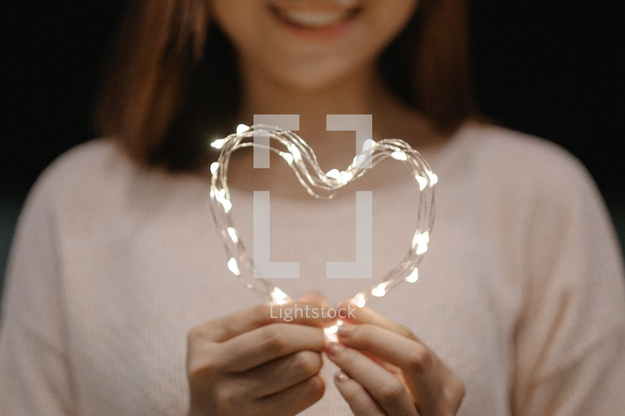 a young woman holding fairy lights in the shape of a heart 