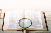 Magnifying glass laying on top of pages of Bible open to Isaiah 12-13 laying on wooden table.
