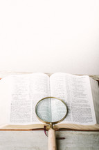 Magnifying glass on top of pages of open Bible.