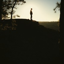 The silhouette of a man standing at the top of a mountain. 