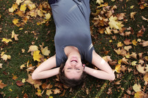 a young woman lying in grass surrounded by fall leaves 