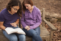 a woman and a young man reading a Bible together 