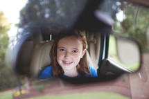 smiling face of a girl child in a rearview mirror 