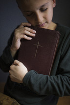 Little boy holding a Bible to his chest.