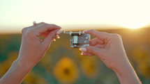 Female hands rotating gears of old music box mechanism. Lady turning the lever of retro small metallic carillon. Woman in sunflowers field listening to music which playing.