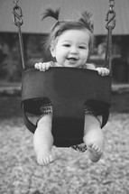 a toddler girl with pigtails in a swing 
