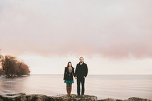 a couple holding hands standing on a rocky shore 