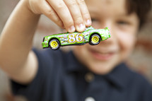 A little boy holds a toy car in front of his face