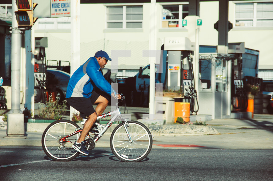 a man riding a bicycle past a gas station 