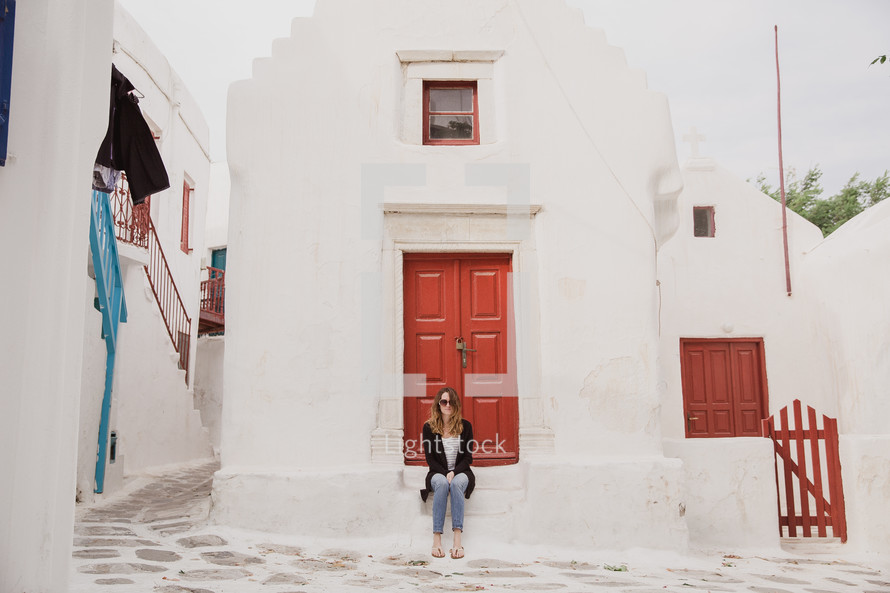 woman sitting on steps in front of a red door in Greece 