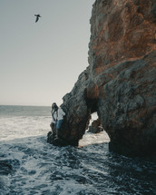 man and woman standing on a large rock formation in the ocean 