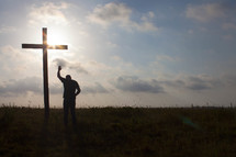 a man with raised hand praying in front of a cross