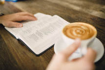 man reading a Bible holding a mug of cappuccino 
