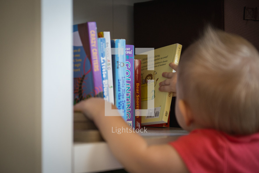 A toddler getting a book off of a bookshelf.