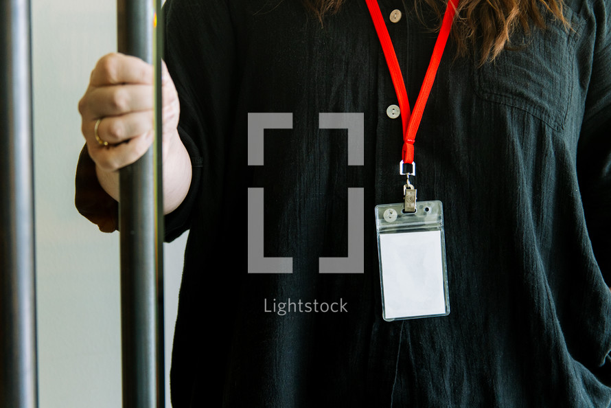 Woman in a black shirt wearing a lanyard while holding a door open.