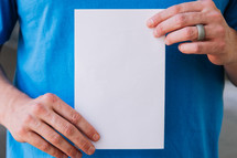 Close up of a man holding up a blank flyer against his torso.