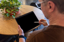 Over the shoulder view of a man holding an iPad pencil against an iPad screen.