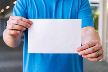 Close up of a man holding up a blank flyer against his torso.