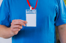 Man in a blank blue tshirt holding up a lanyard.