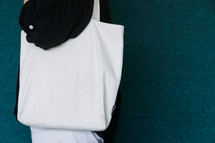 Woman in a black shirt holding a blank canvas tote bag on her shoulder.