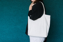 Woman in a black shirt holding a blank canvas tote bag on her shoulder.