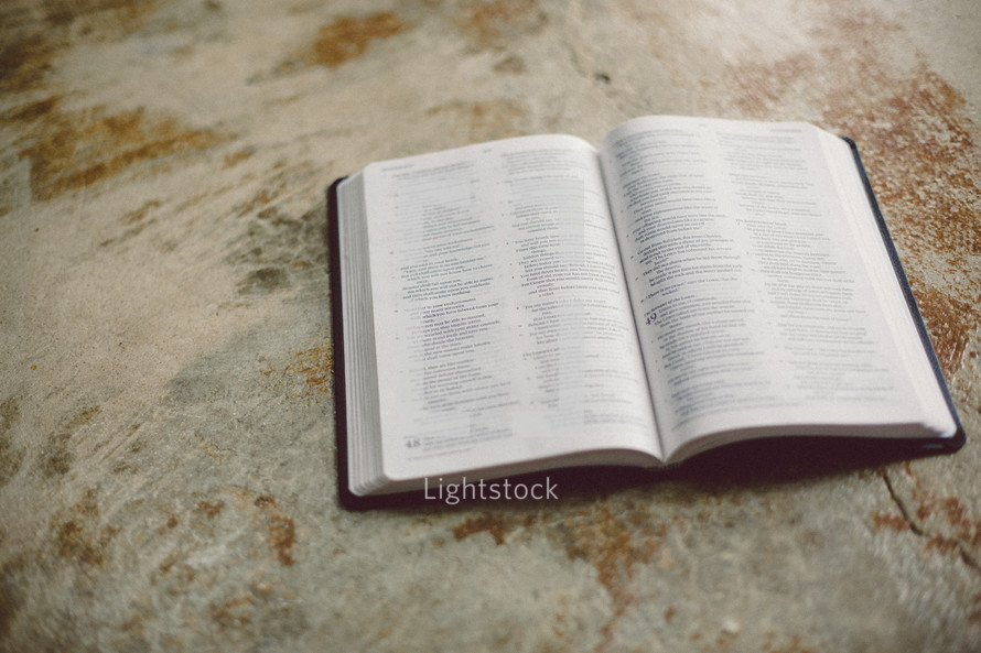 Open Bible on a concrete floor.
