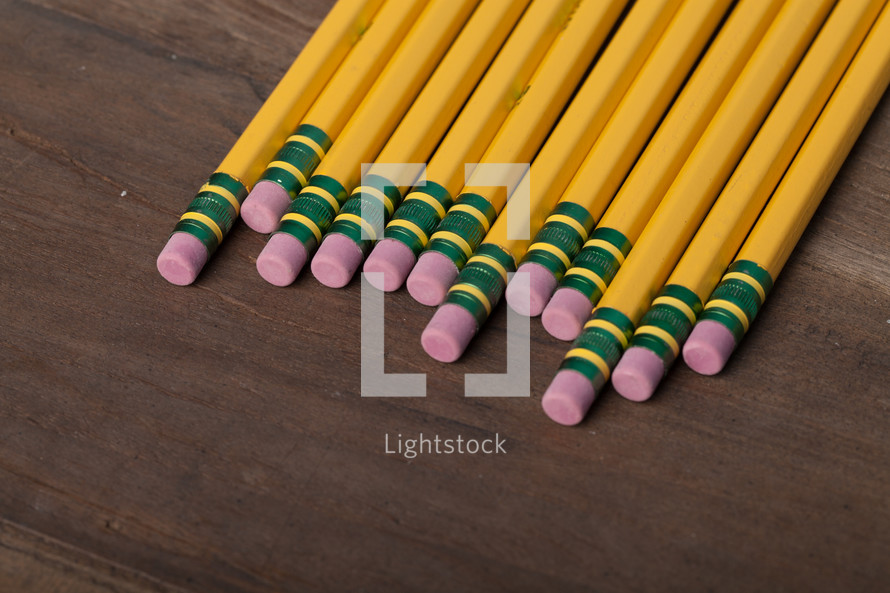 A row of yellow wooden pencils on a wooden surface.