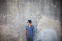 man listening to earbuds standing in front of a gray wall with graffiti 