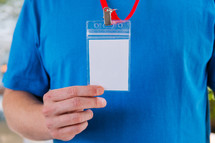 Man in a blank blue tshirt holding up a lanyard.