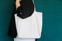 Woman in a black shirt holding a blank canvas tote bag on her shoulder.