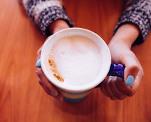 A woman's hands holding a cup of cappuccino.
