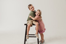 boy child sitting on a stool hugging his sister 